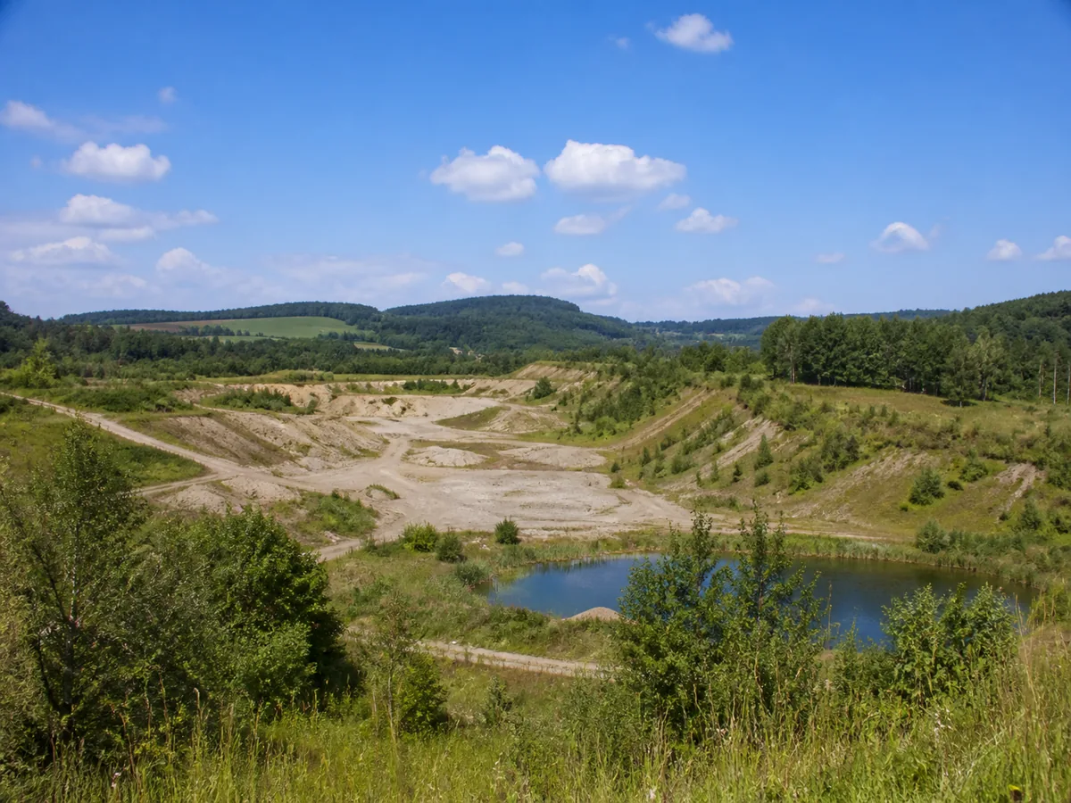 Frühere österreichische Abbaufläche mit begrünten Böschungen und kleinem Wasserbereich